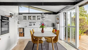 A modern kitchen with white cabinetry, a dining area with a table and chairs, and large windows offering a view of the outdoors. - Awesome home in Sydals with WiFi (Sydals)