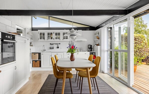 A modern kitchen with white cabinetry, a dining area with a table and chairs, and large windows offering a view of the outdoors. - Nice home in Sydals with WiFi (Sydals)