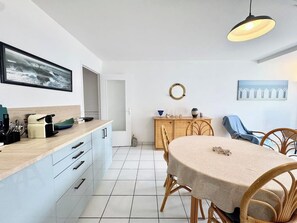A modern kitchen with a dining area, featuring a large island, white cabinetry, and a round table with chairs. - Lovely ! T2 Top Cosy - Terrasse (Quiberon)