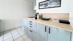 A modern kitchen with a light wood countertop, a framed picture above the sink, and a small coffee machine.