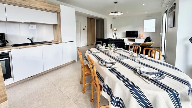 Une cuisine moderne avec des meubles blancs, un plan de travail en bois et un coin repas agrémenté d’une nappe à rayures.