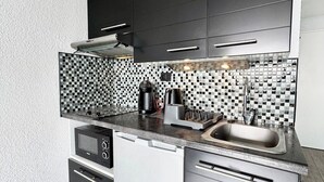 A modern kitchen with black cabinets, a tiled backsplash, and stainless steel appliances. - Studio Confort - Vue sur Mer - Balcon (Guidel)