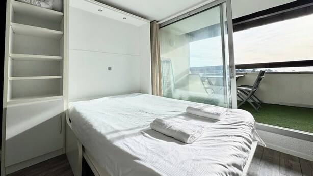 A bedroom with a bed, a built-in wardrobe, and a balcony with a view. - Studio Confort - Vue sur Mer - Balcon (Guidel)