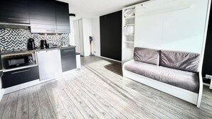 A modern kitchen with built-in appliances, a grey sofa, and a white wardrobe. - Studio Confort - Vue sur Mer - Balcon (Guidel)