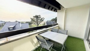 A balcony with a table and chairs, green artificial grass, and a view of houses and trees. - Studio Confort - Vue sur Mer - Balcon (Guidel)