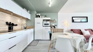 Una cuina moderna amb armaris blancs, un taulell de fusta i una zona de menjador amb taula i cadires.