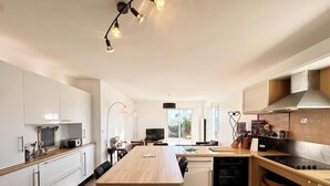 A modern kitchen with white cabinets, a wooden dining table, and a built-in oven.