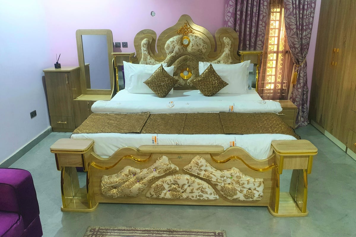 A bedroom with a large bed, a wooden nightstand, a dresser, and a mirror.