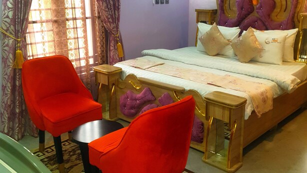 A bedroom with a bed, two red chairs, a small table, and an air conditioning unit on the wall. - Bly & Schol Apartments (Abuja)