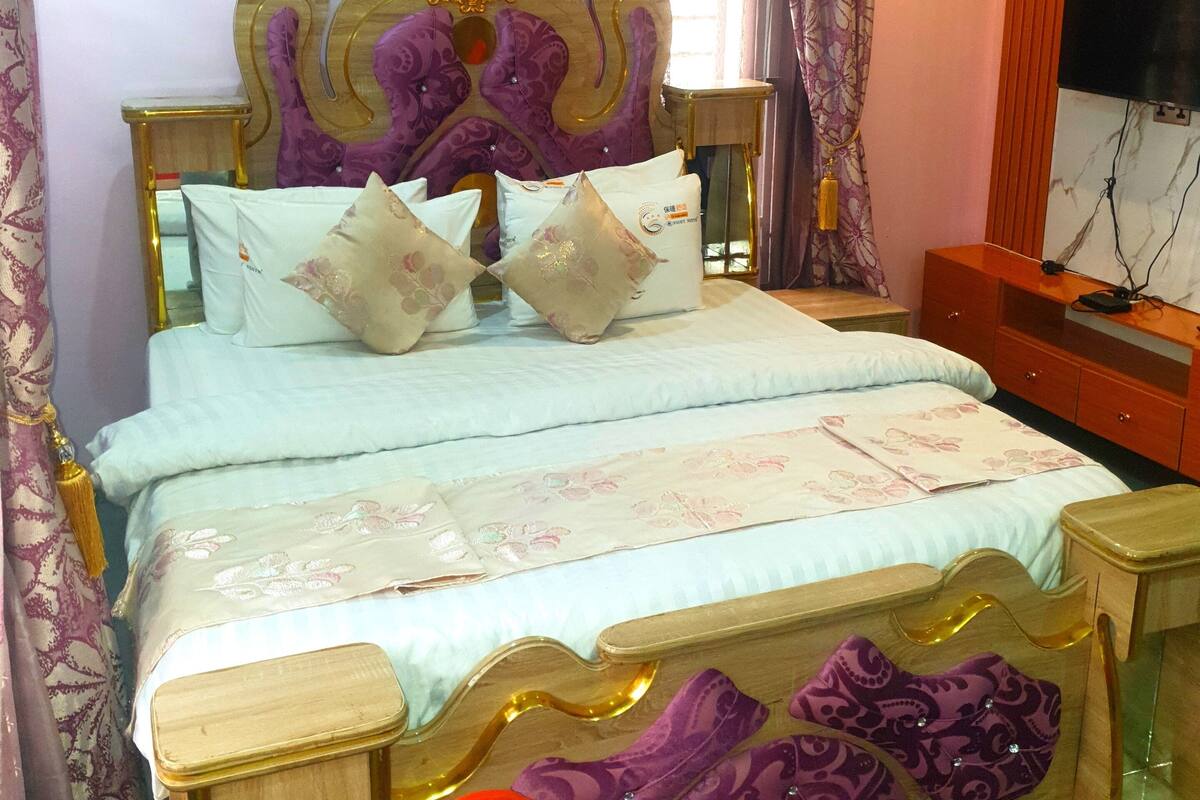 A bedroom with a bed, a nightstand, a TV, and an air conditioner.