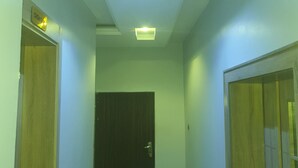 A hallway with two wooden doors, a dark door at the end, and a ceiling light fixture. - Bly & Schol Apartments (Abuja)