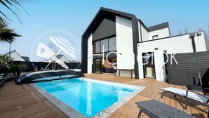 Uma casa moderna com piscina, um alpendre com cadeiras de descanso e uma janela grande.