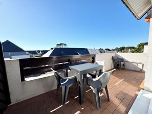 Een terras op het dak met een tafel en stoelen, een houten bankje en uitzicht op omliggende gebouwen.