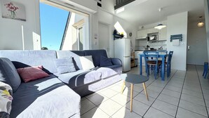 Una sala de estar moderna con un sofá, una mesita y una cocina con mesa y sillas.