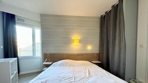 A hotel room with a large bed, a bedside table, a lamp, and a window with curtains.