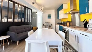 A modern kitchen with white cabinets, a grey sofa, and a dining table.