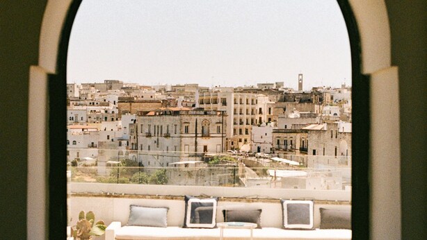 Vista desde una ventana que muestra un paisaje urbano con edificios, una torre del reloj y cielo despejado.