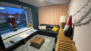 Een gezellige woonkamer met een bank, een houten salontafel en een raamzitplaats met kussens.