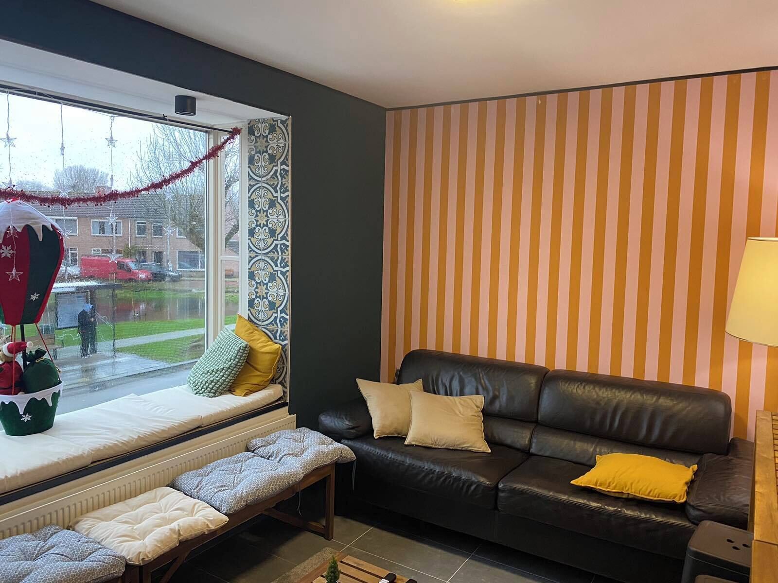Un salon avec un canapé en cuir noir, un banc et un siège de fenêtre agrémenté de coussins.