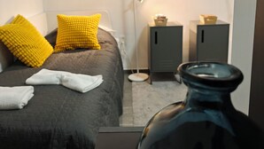 Een slaapkamer met een bed, kussens, een nachtkastje, een lamp en een kast.