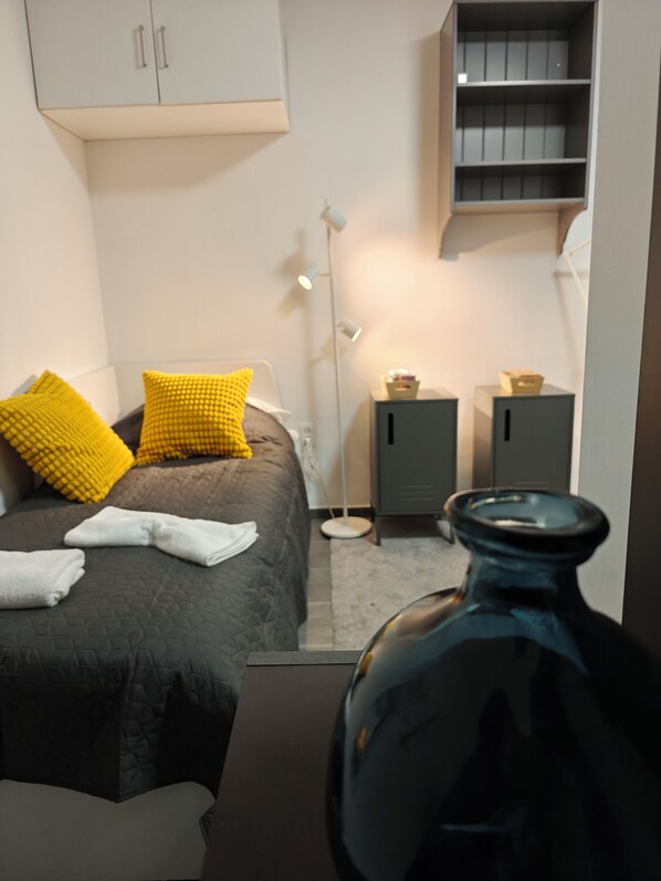 Un dormitorio con cama, almohadas, mesita de noche, lámpara y armario.