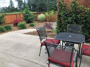 Un patio con una mesa y sillas de metal, rodeado por una valla de madera y diversas plantas.