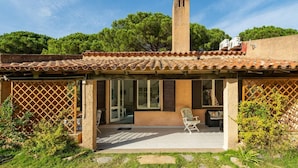Una casa con techo de tejas, chimenea y un porche cubierto con una silla y una mesa.