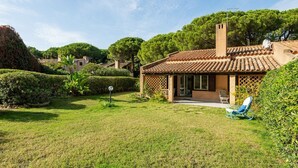 Una casa con techo de tejas, chimenea y jardín con césped y setos.