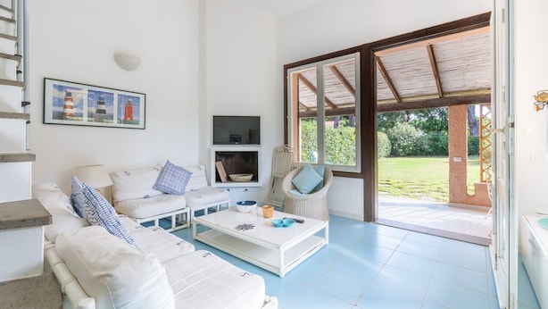 Un salón amplio con un sofá blanco, una mesa de centro y un televisor. Una ventana grande ofrece vistas al exterior.