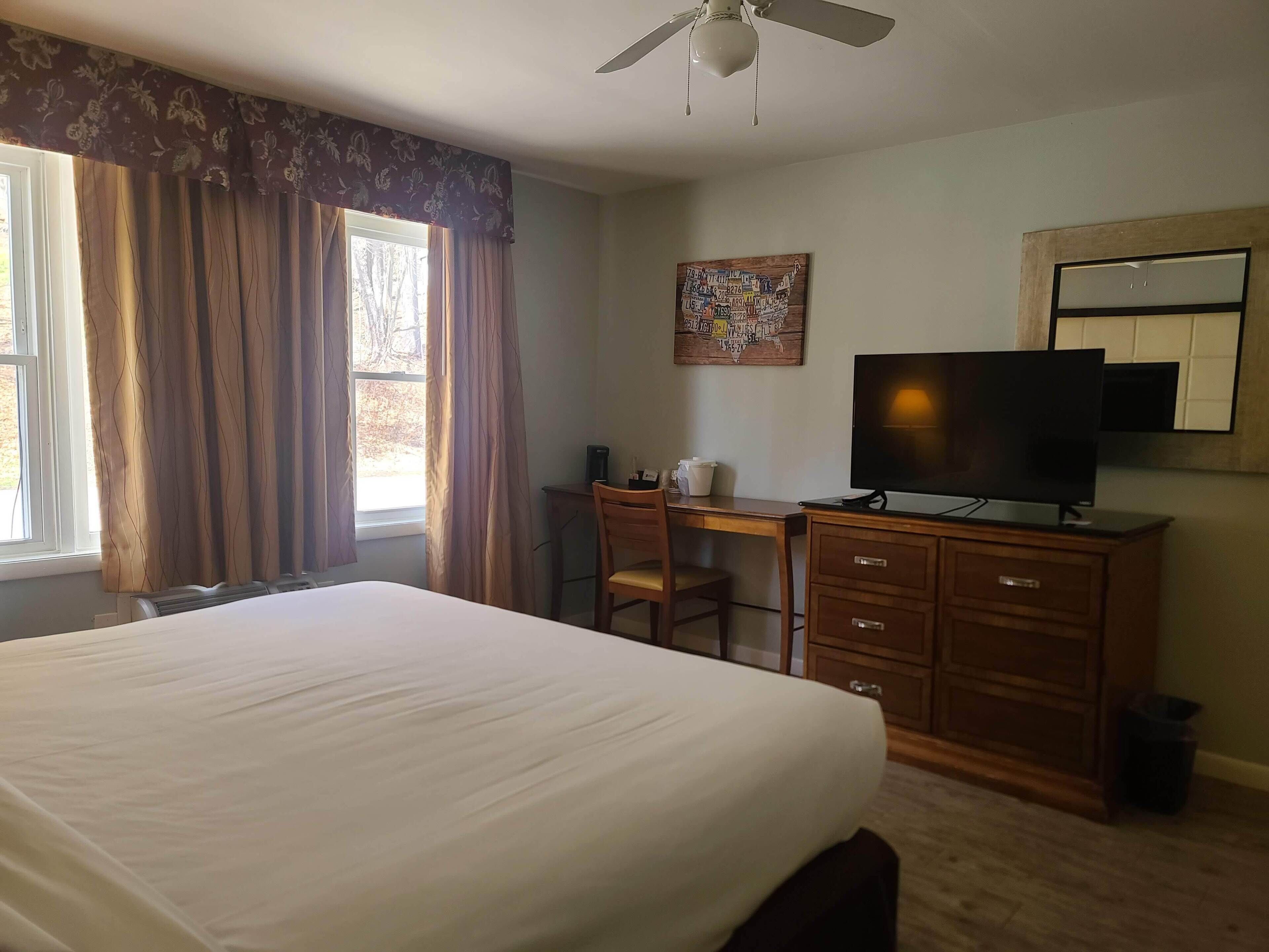 A hotel room with a large bed, a desk with a chair, a television, and a ceiling fan.