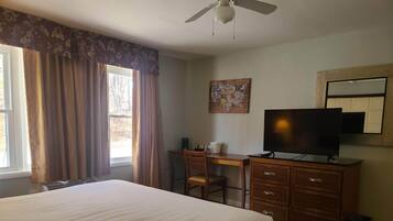 A hotel room with a large bed, a desk with a chair, a television, and a ceiling fan.