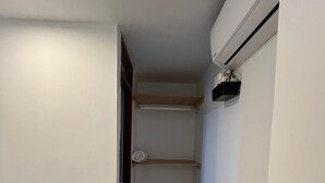 Un couloir étroit, avec une étagère intégrée le long du mur, une porte à gauche et un appareil de climatisation à droite.