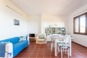 A living room with a blue sofa, a white dining table with chairs, a bookshelf, and a television.