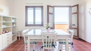 A dining area with a white table and chairs, a small potted plant, and a view of the sea through a window. - Casa del Lentischio (Funtana Meiga)