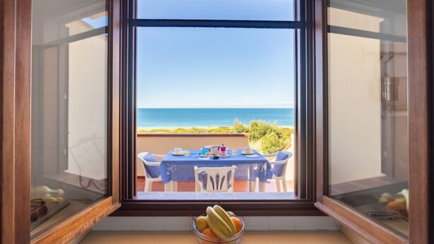 A dining area with a table and chairs, a bowl of fruit, and a view of the ocean. - Casa del Lentischio (Funtana Meiga)