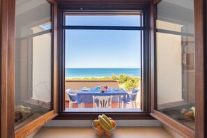 A dining area with a table and chairs, a bowl of fruit, and a view of the ocean.