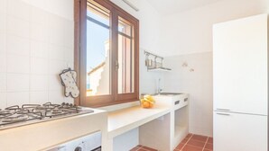 A compact kitchen with a gas stove, a window, and a white refrigerator. - Casa del Lentischio (Funtana Meiga)