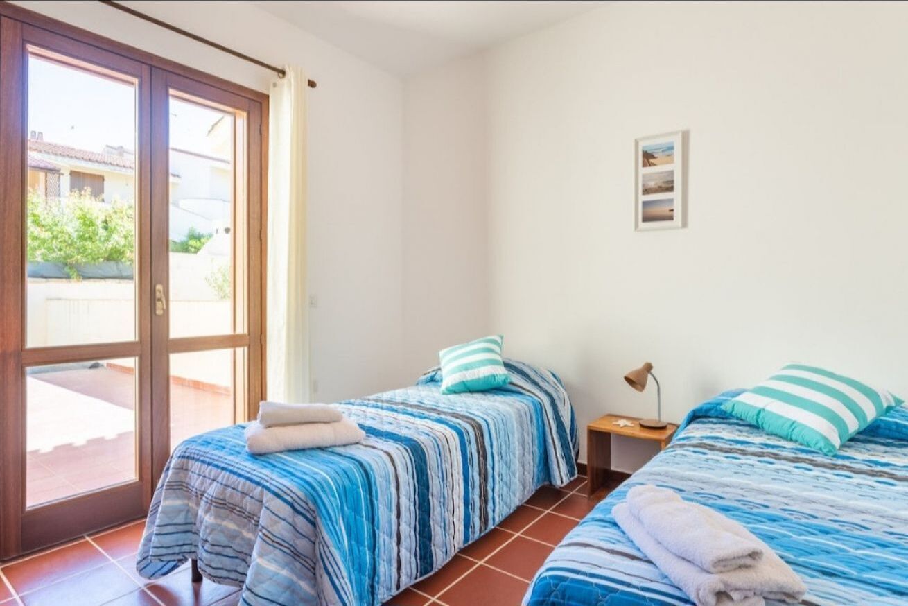 A bedroom with two beds, a sliding glass door, and a small bedside table with a lamp.