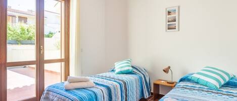 A bedroom with two beds, a sliding glass door, and a small bedside table with a lamp.