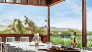 An outdoor dining area with a table set for two, featuring a bottle of wine, nuts, and a bowl of fruit. - The Deck at Sellicks ~ Family friendly entertainer (Sellicks Beach)