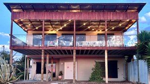 A two-story building with a flat roof, a covered patio area with outdoor seating, and a small garden with stepping stones. - The Deck at Sellicks ~ Family friendly entertainer (Sellicks Beach)