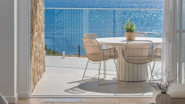 A balcony with a table and chairs, a potted plant, and a view of the ocean. - Horizons ~ Designer luxury stay with dream views (Aldinga Beach)