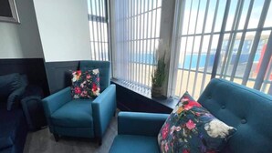A modern interior with a blue sofa, matching armchair, and a window with blinds. - Serenity Wembley (Blackpool)