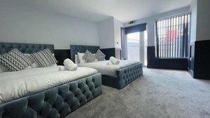 A hotel room with two beds, a large window with blinds, and a carpeted floor. - Serenity Wembley (Blackpool)