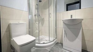 A bathroom with a toilet, a glass-enclosed shower, and a sink. - Serenity Wembley (Blackpool)