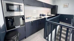 A modern kitchen with a microwave, oven, and sink. There is a staircase leading to an upper level. - Serenity Wembley (Blackpool)