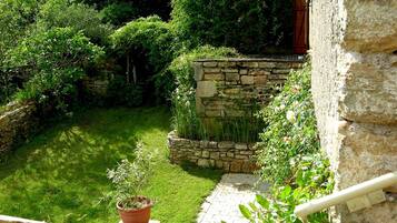 Un muro de piedra con una planta en maceta y un pequeño jardín con césped y arbustos.