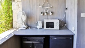 Une cuisine compacte avec un mur en bois, un micro-ondes blanc, une bouilloire et un ventilateur.