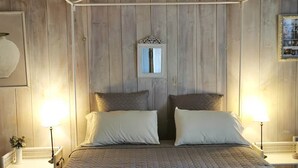 Une chambre à coucher avec une tête de lit en bois, deux tables de chevet avec des lampes, un grand lit recouvert d’une courtepointe, et un miroir au mur.