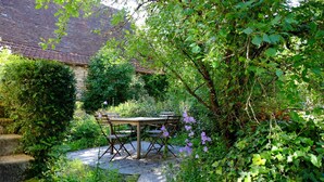 A garden with a stone pathway leading to a wooden table and chairs.
